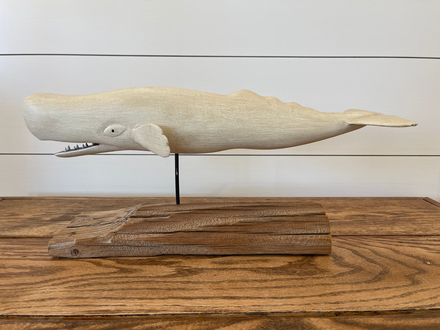 Wooden whale sculpture on a wooden base against a white wall