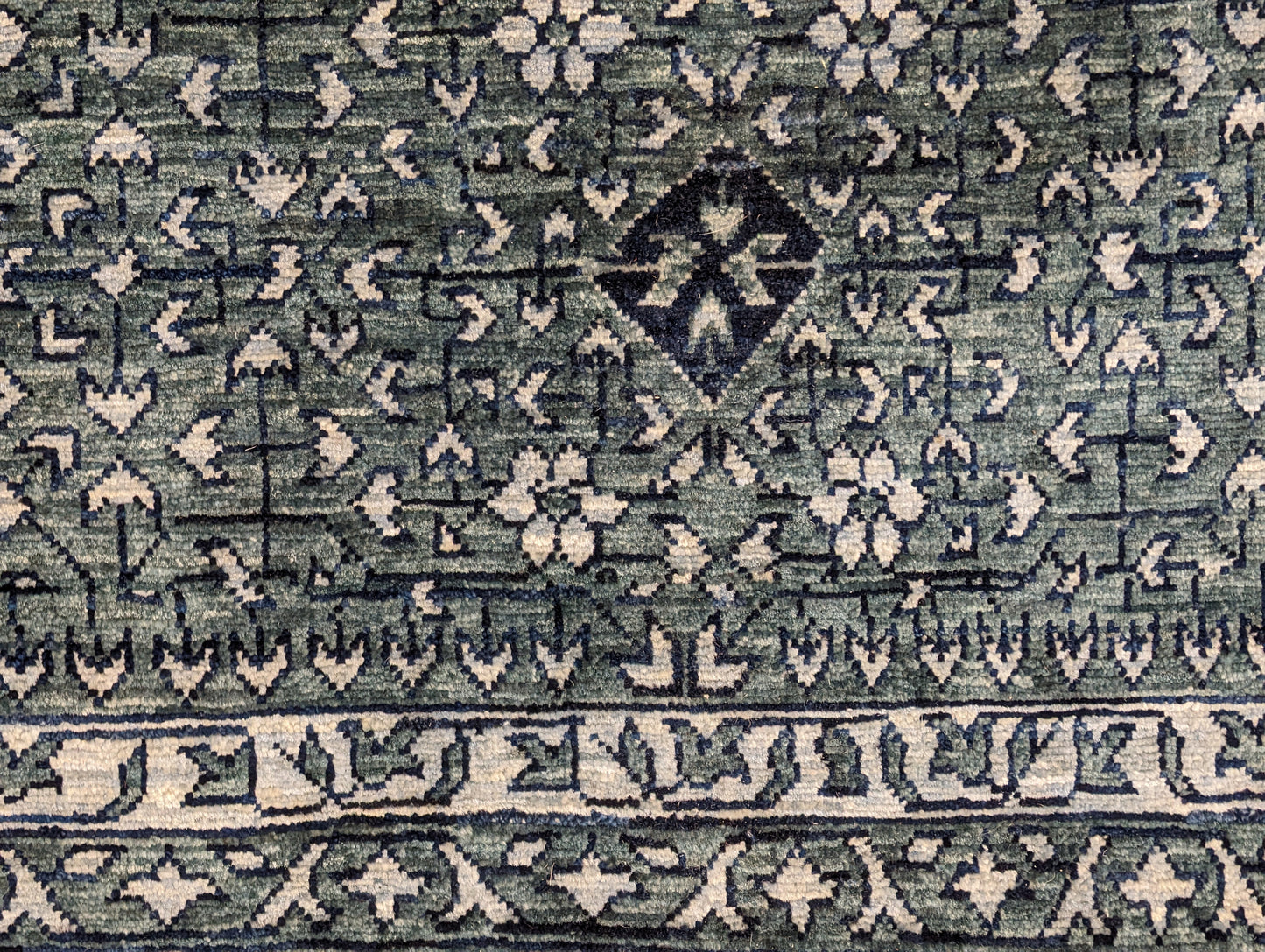 A hand-knotted wool rug with a geometric pattern in smokey green, deep navy, and crisp ivory colors.