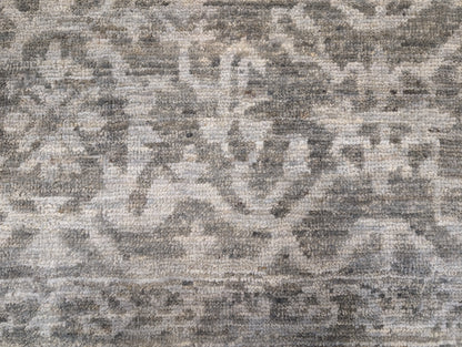 A hand-knotted wool rug with a subtle grey color palette, featuring intricate geometric patterns.