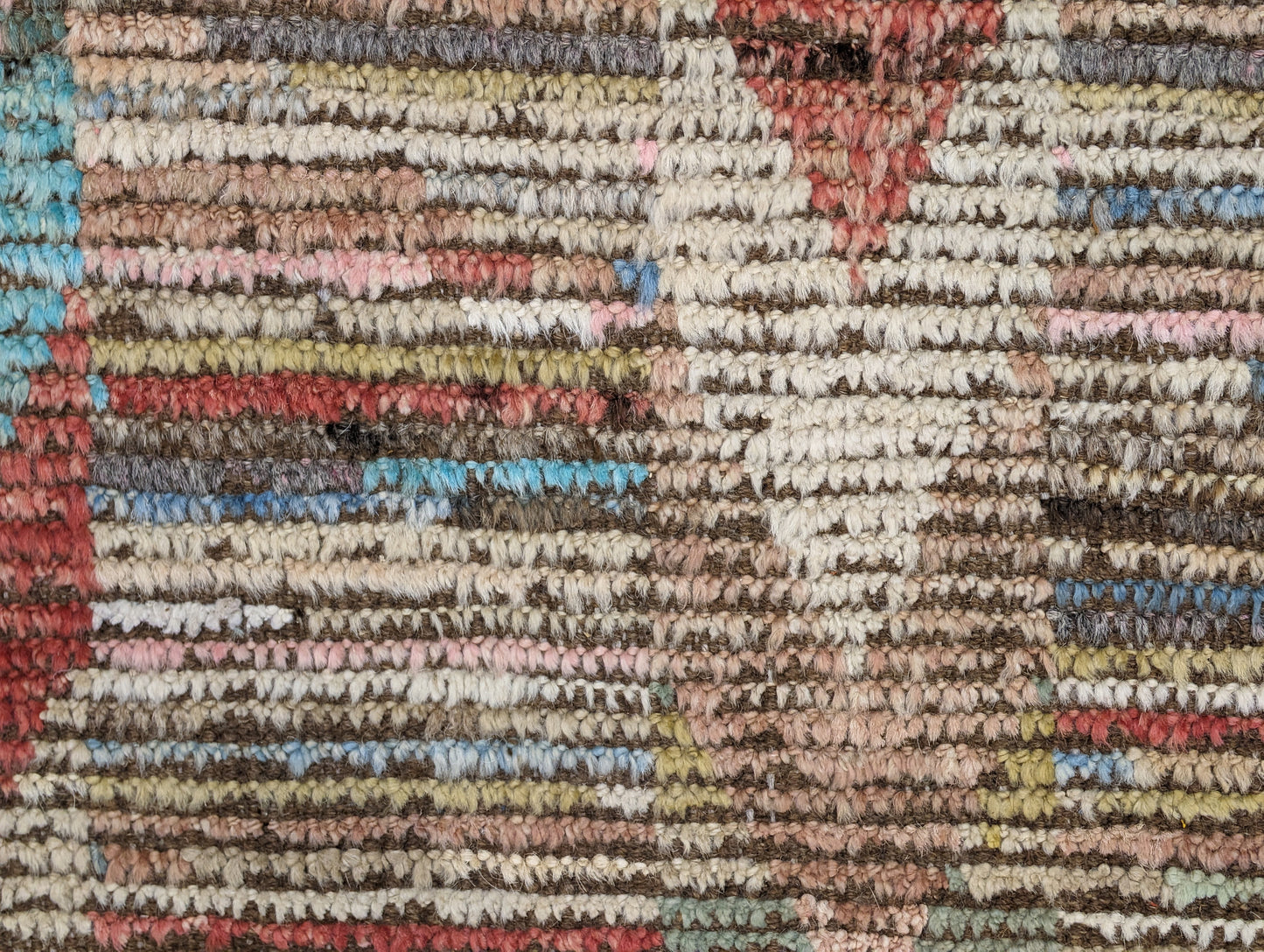 A hand-knotted wool rug with a coastal aesthetic in a plush design, featuring a mix of pink, red, yellow, blues, browns, and ivory colors.