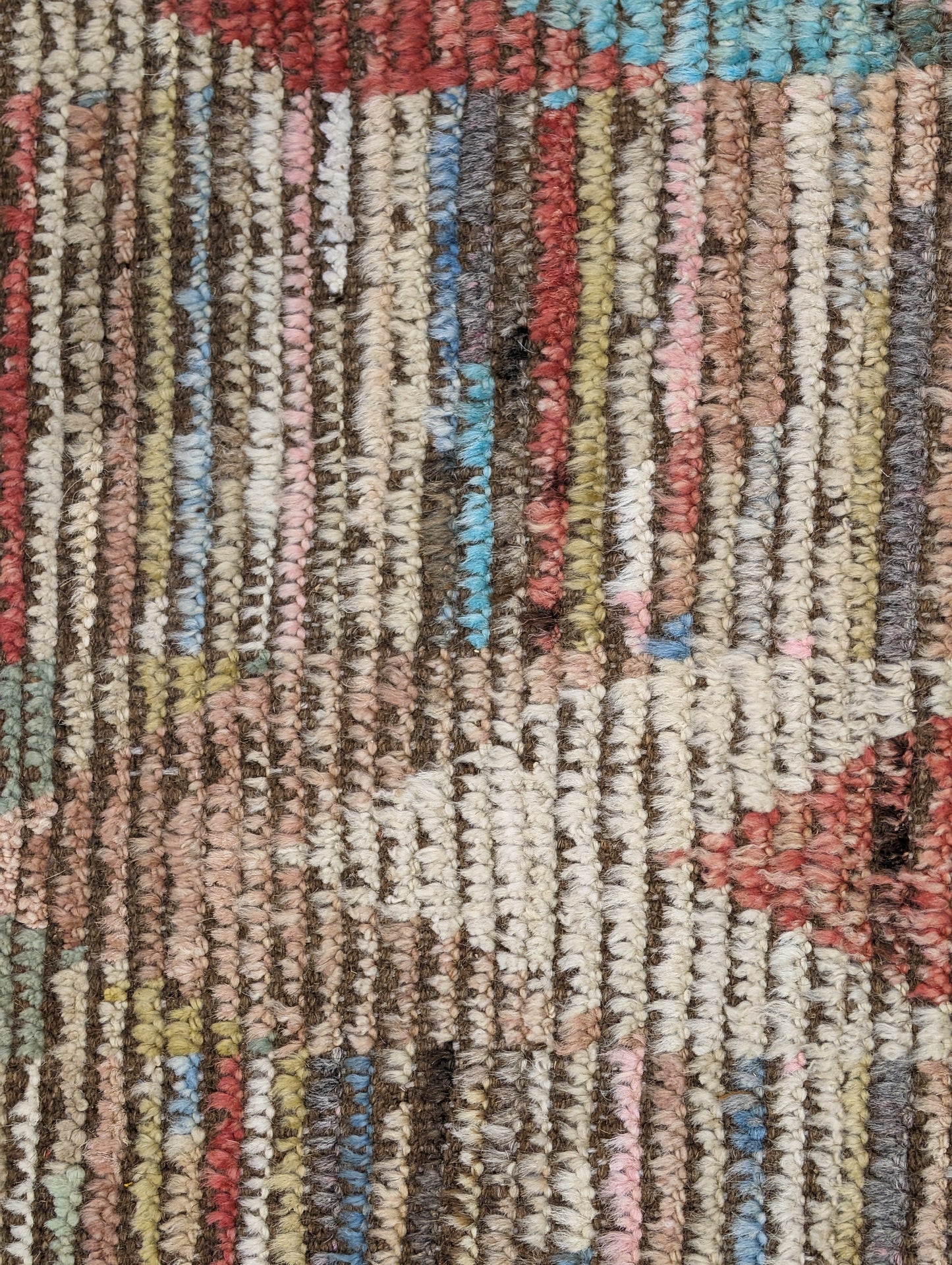 A hand-knotted wool rug with a coastal aesthetic in a plush design, featuring a mix of pink, red, yellow, blues, browns, and ivory colors.
