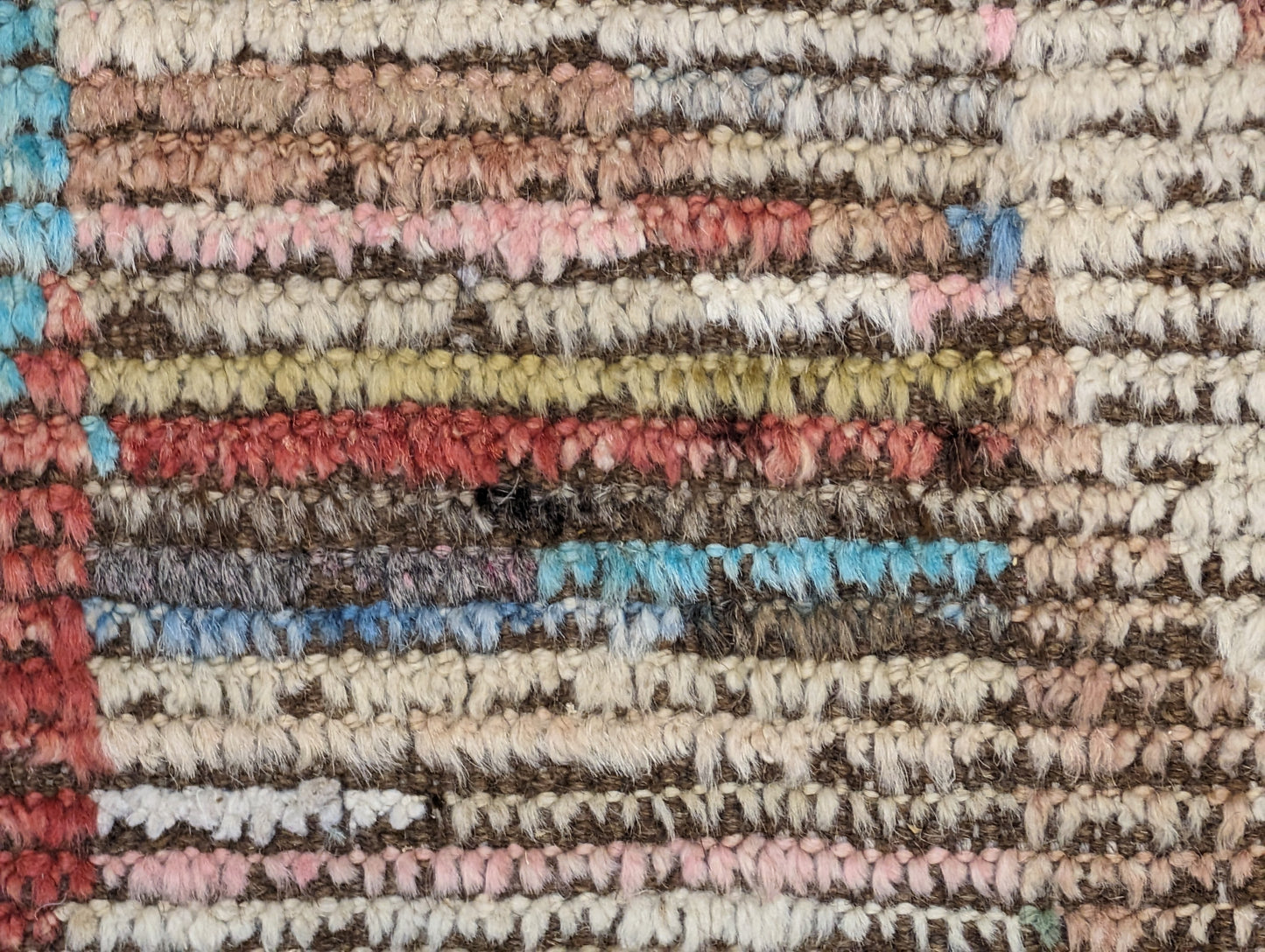A hand-knotted wool rug with a coastal aesthetic in a plush design, featuring a mix of pink, red, yellow, blues, browns, and ivory colors.