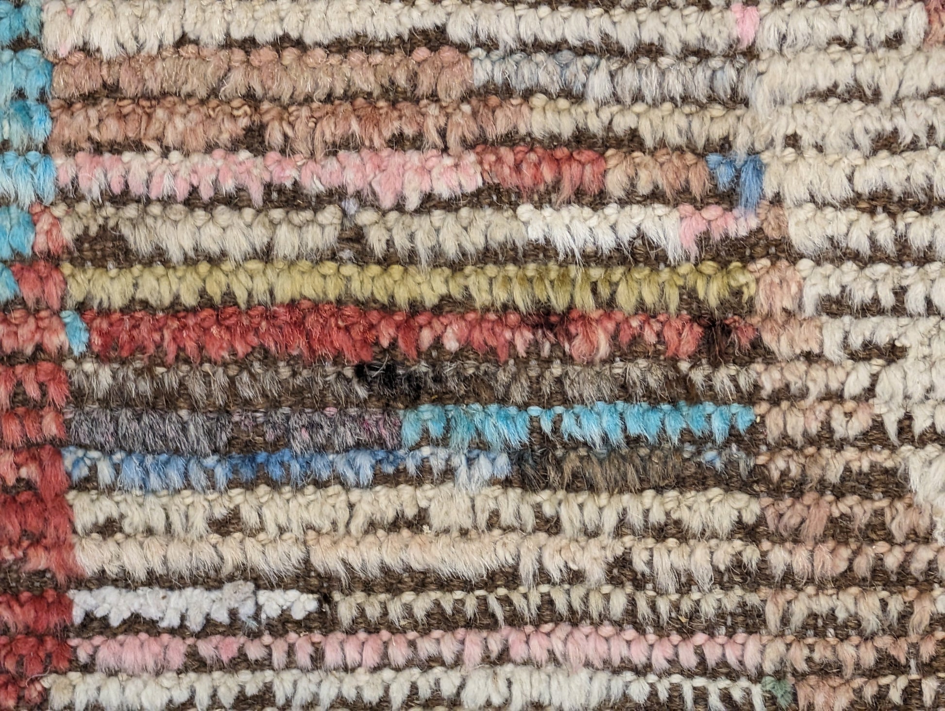 A hand-knotted wool rug with a coastal aesthetic in a plush design, featuring a mix of pink, red, yellow, blues, browns, and ivory colors.