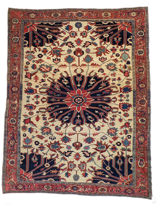 A hand-knotted wool rug with a traditional Serapi design, featuring a luxurious palette of ink blue, warm reds, green, pink, gold, blue, and ivory.