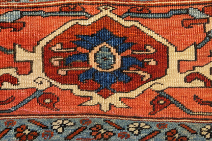 A hand-knotted wool rug with a traditional Serapi design, featuring a luxurious palette of ink blue, warm reds, green, pink, gold, blue, and ivory.