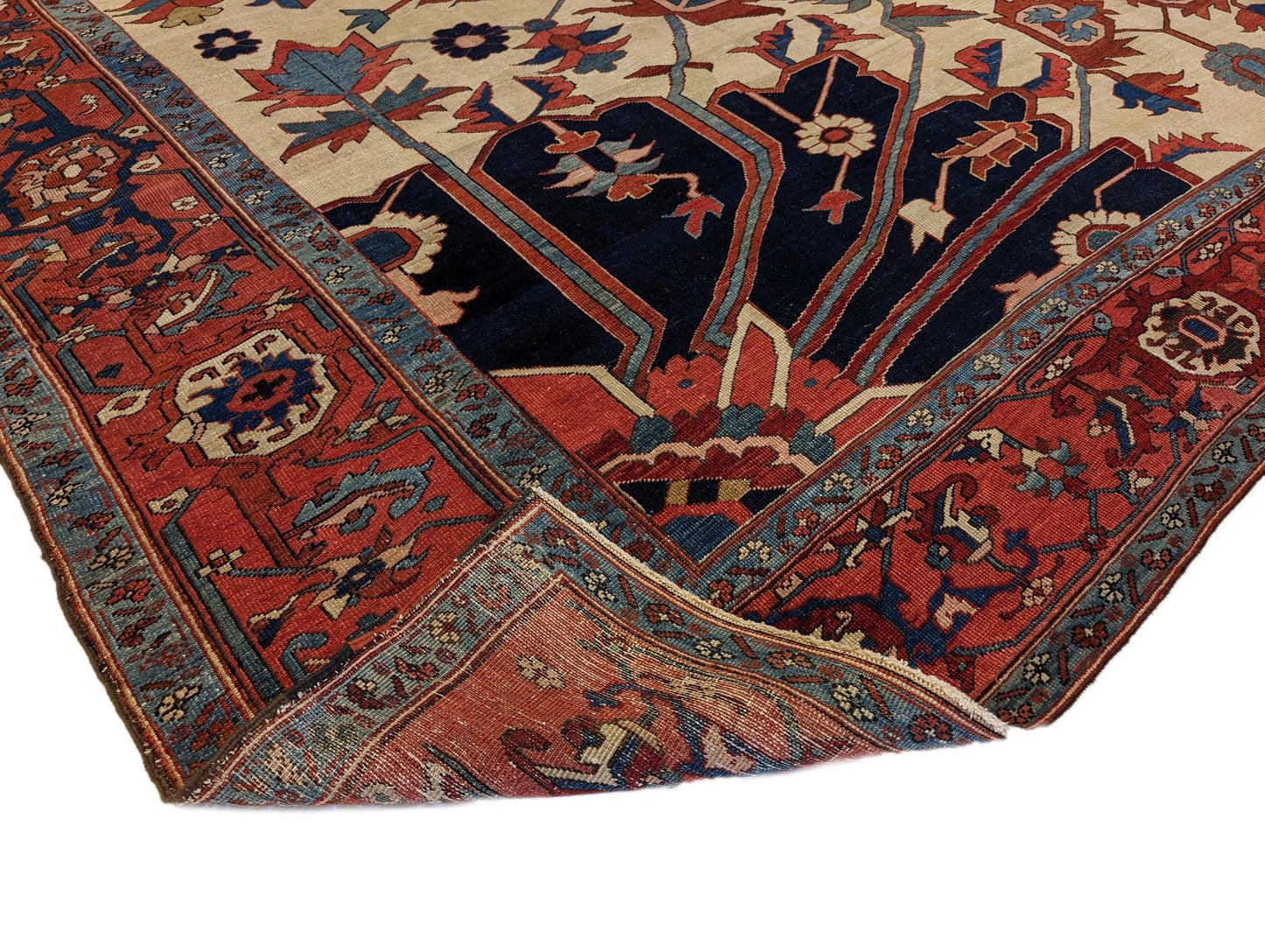 A hand-knotted wool rug with a traditional Serapi design, featuring a luxurious palette of ink blue, warm reds, green, pink, gold, blue, and ivory.
