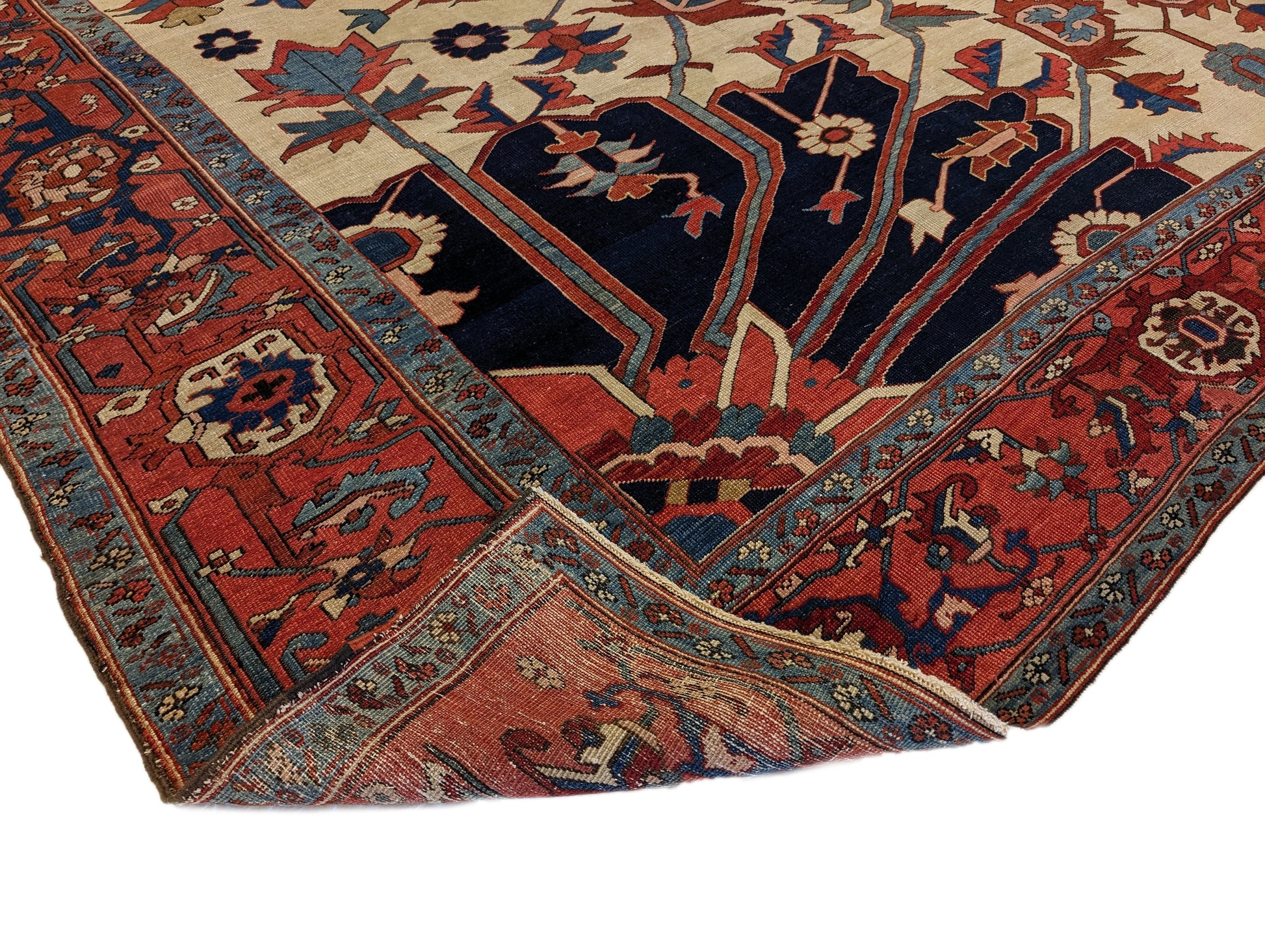 A hand-knotted wool rug with a traditional Serapi design, featuring a luxurious palette of ink blue, warm reds, green, pink, gold, blue, and ivory.
