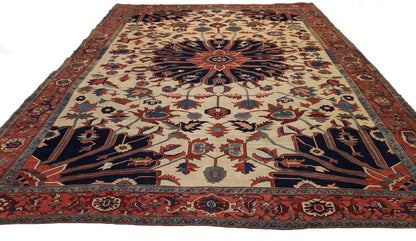 A hand-knotted wool rug with a traditional Serapi design, featuring a luxurious palette of ink blue, warm reds, green, pink, gold, blue, and ivory.