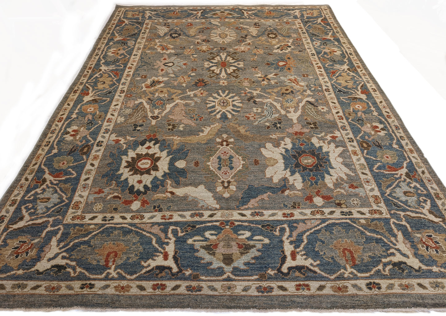 A hand-knotted wool rug with a traditional and contemporary design, featuring a rich palette of colors including slate grey, red, gold, pink, blue, green, and beige, and decorative border patterns.