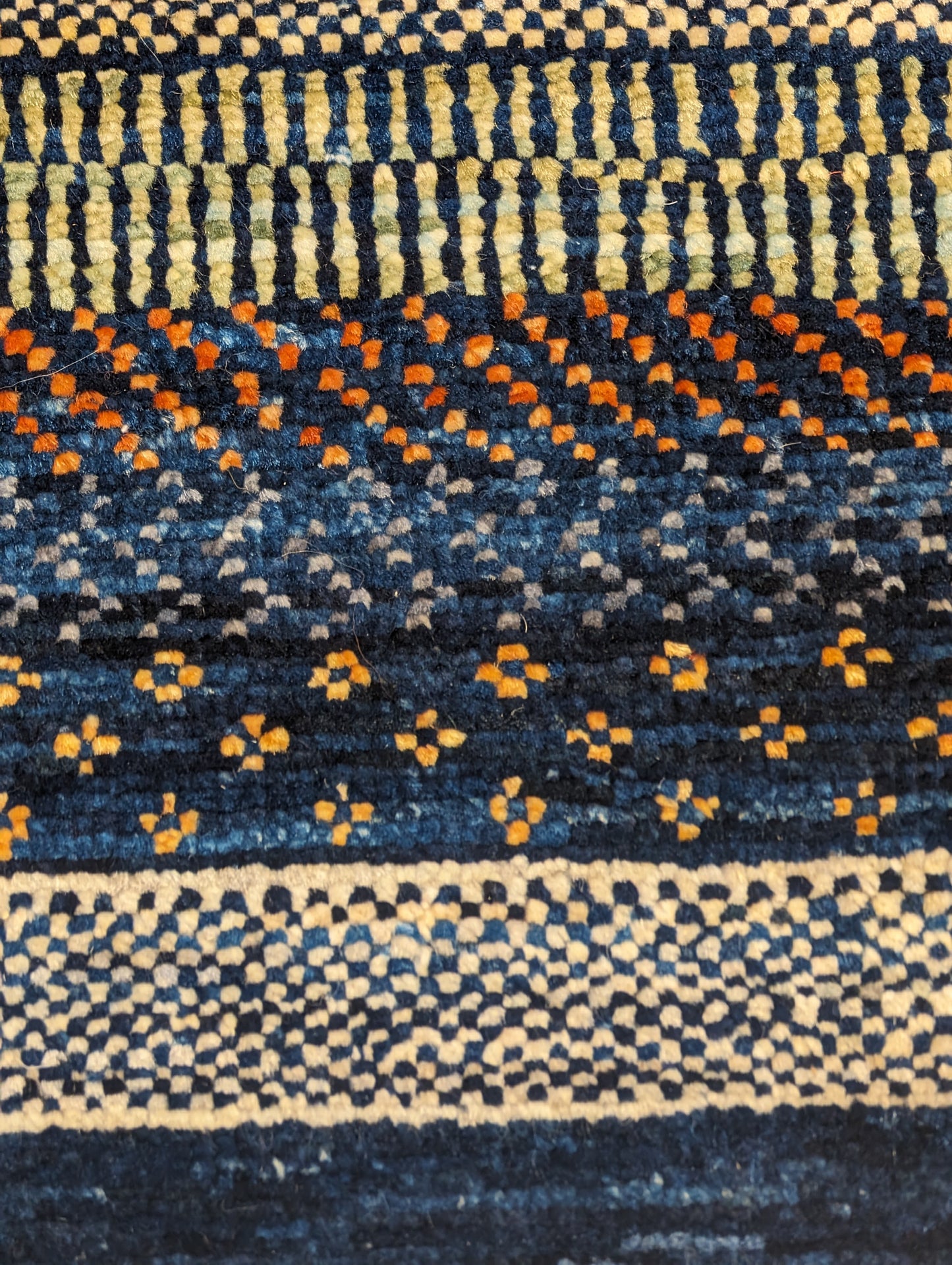 A hand-knotted wool rug with a geometric pattern in a variety of coastal hues including deep navy blue, red, warm orange, green, cheerful yellow, and soft ivory. Cozy pile. 