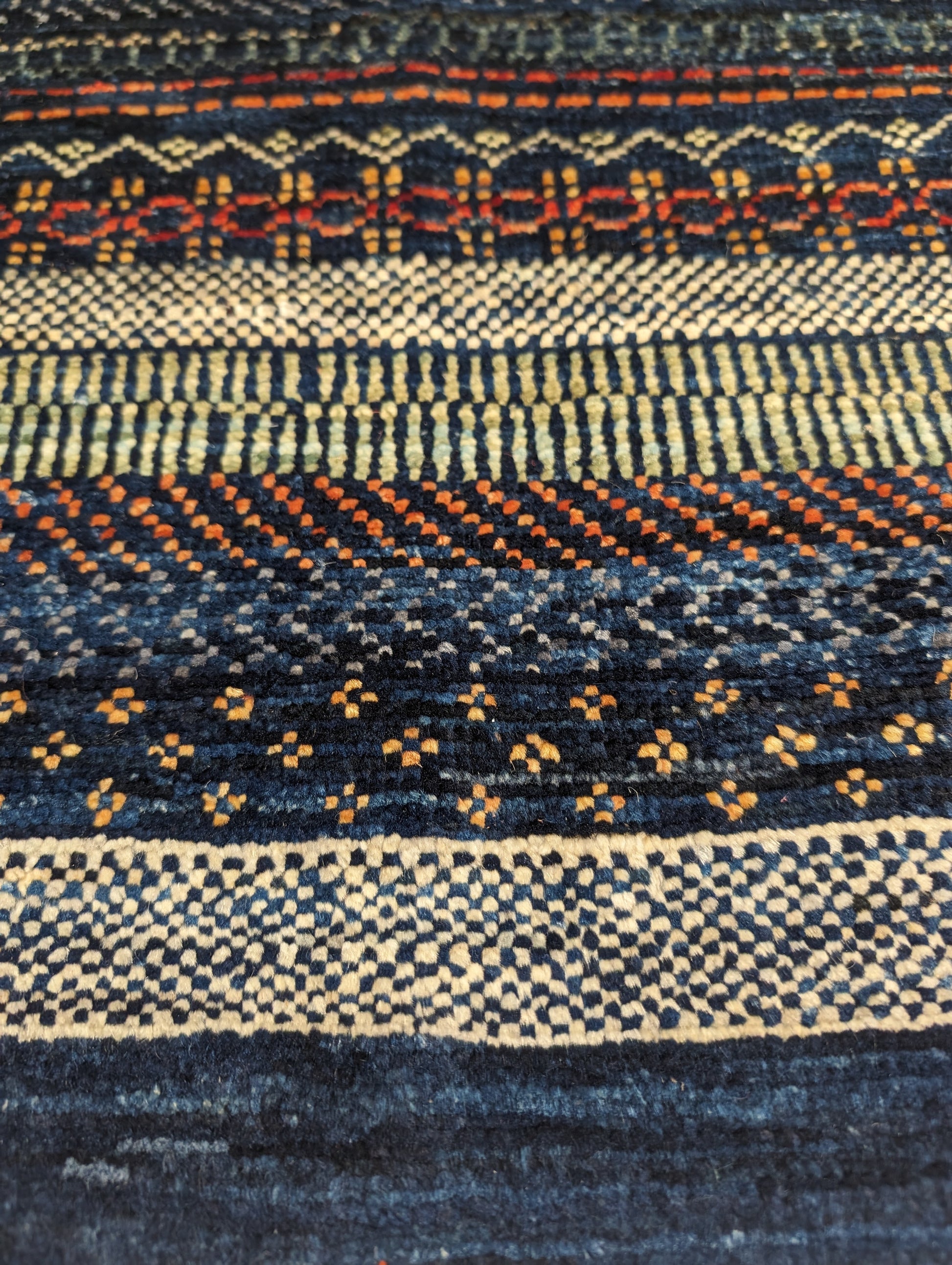 A hand-knotted wool rug with a geometric pattern in a variety of coastal hues including deep navy blue, red, warm orange, green, cheerful yellow, and soft ivory. Cozy pile. 
