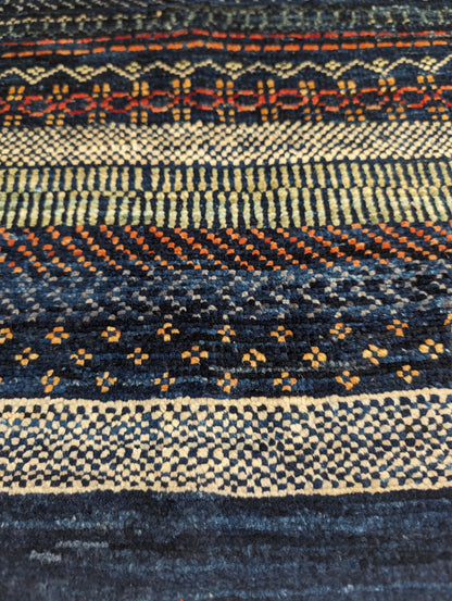 A hand-knotted wool rug with a geometric pattern in a variety of coastal hues including deep navy blue, red, warm orange, green, cheerful yellow, and soft ivory. Cozy pile. 