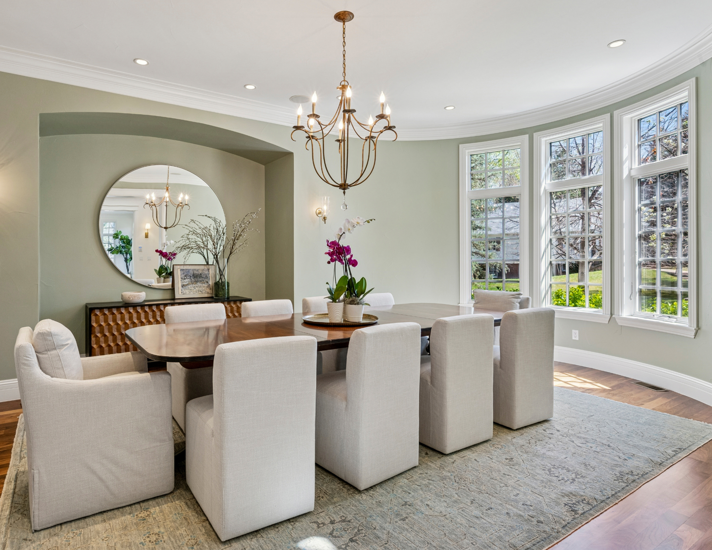 Dining room with a wooden table, white chairs, and a chandelier. The space is anchored by a cozy rug that perfectly unifies the décor.