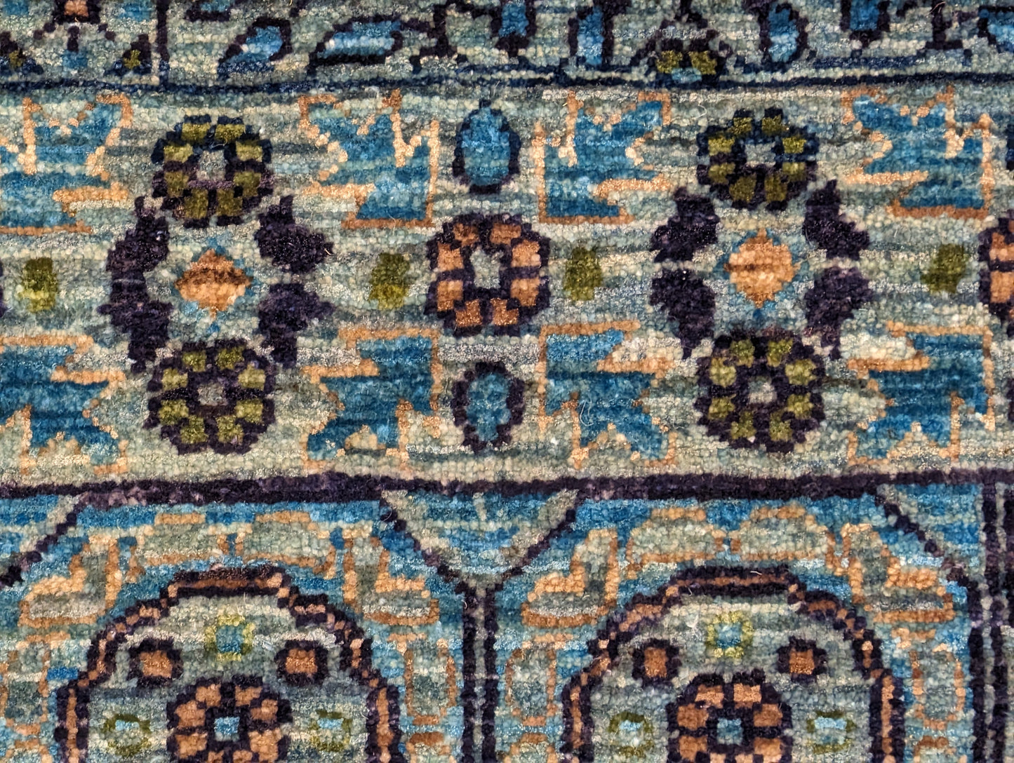 A hand-knotted wool rug with a vivid palette of colors including turquoise, orange, green, eggplant, grey, and navy, featuring intricate tribal patterns.