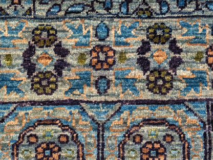 A hand-knotted wool rug with a vivid palette of colors including turquoise, orange, green, eggplant, grey, and navy, featuring intricate tribal patterns.