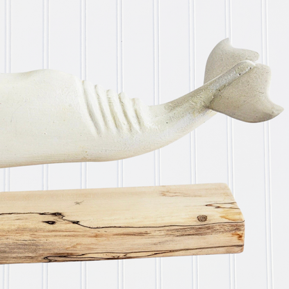 Decorative whale sculpture on a wooden shelf against a white paneled wall