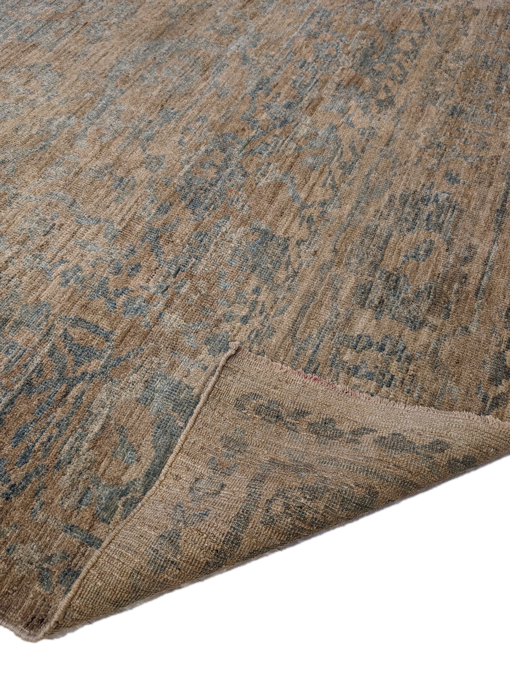 A hand-knotted low pile wool rug with a coastal-inspired design in natural tones of sandy brown and a subtle hint of aquamarine.