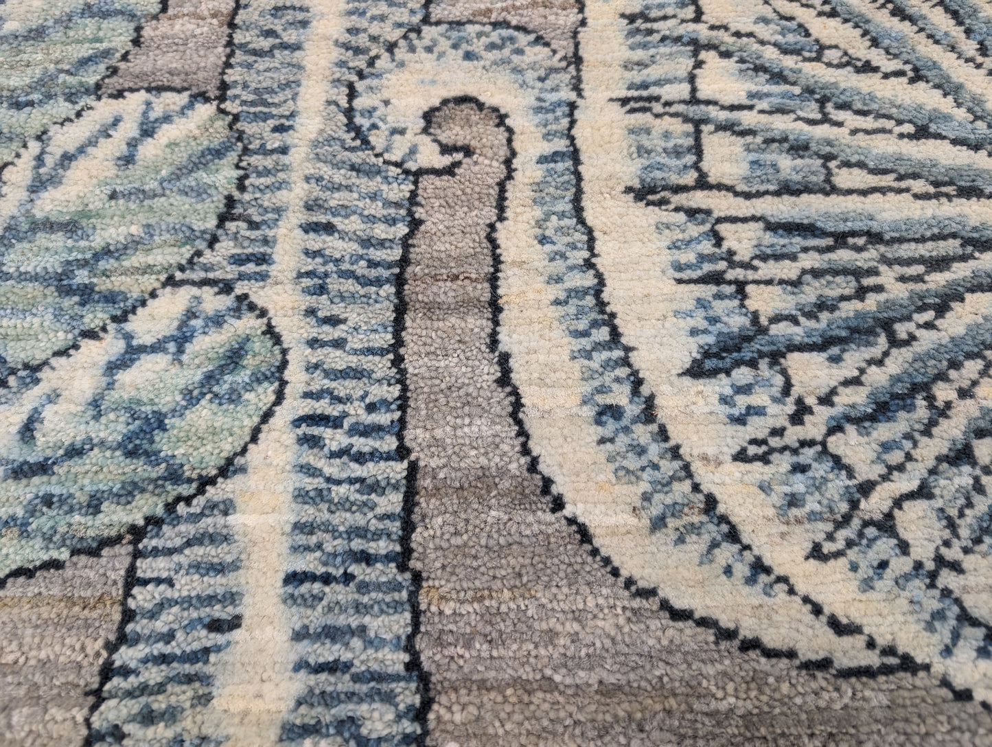A hand-knotted wool rug with a coastal-inspired floral and plant design in shades of beige, gray, blue, green, and black.