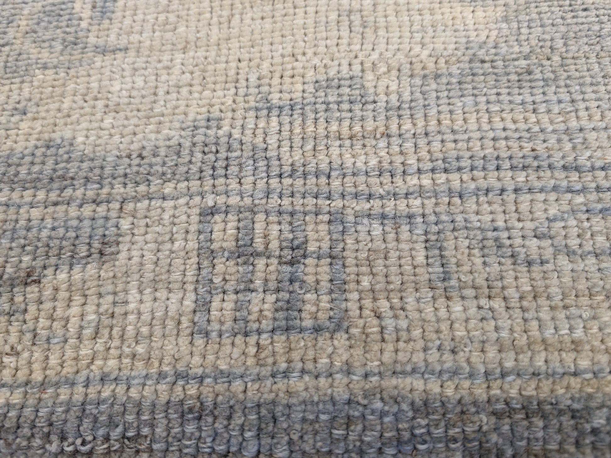 An antique-style beige and neutral-colored rug with a floral and geometric pattern, hand-knotted with low pile.