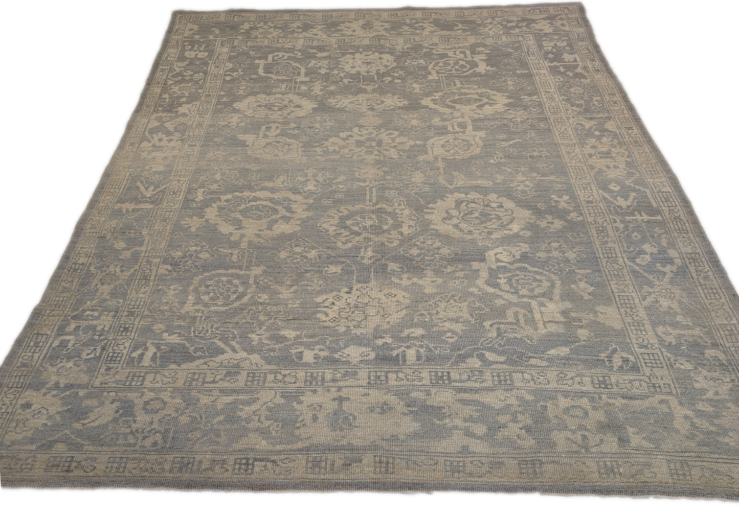 An antique-style beige and neutral-colored rug with a floral and geometric pattern, hand-knotted with low pile.