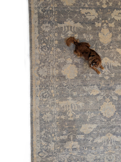 A hand-knotted wool rug with a coastal-inspired design in shades of ivory, beige, grey, blue, smokey green, light yellow, and soft brown. Ollie Pickles laying on rug. 