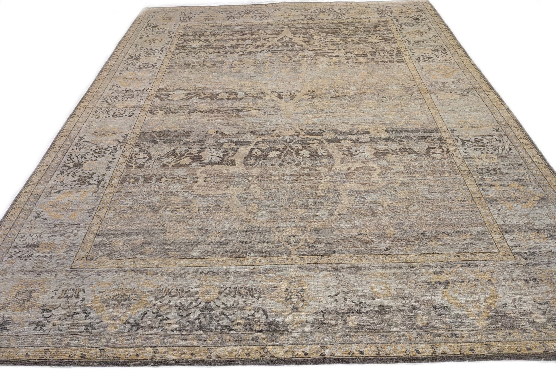 A handwoven rug with a beige and brown color palette with accents of yellow and faded blue, featuring geometric and floral patterns.