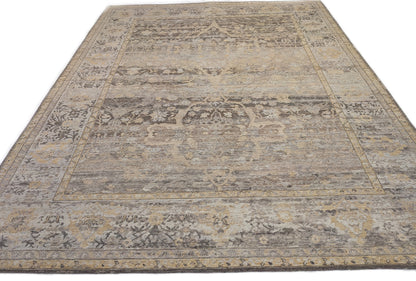 A handwoven rug with a beige and brown color palette with accents of yellow and faded blue, featuring geometric and floral patterns.