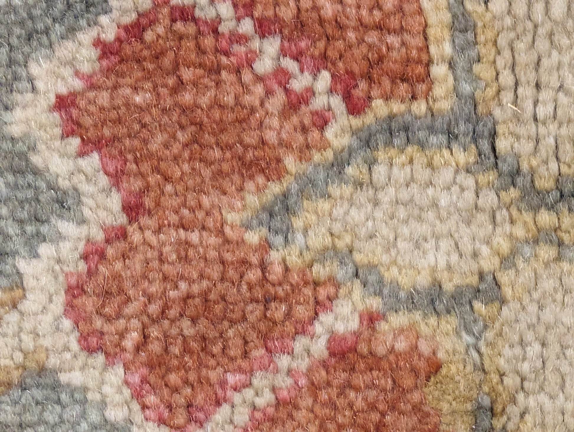 A handmade rug with a classic geometric pattern featuring a mix of rosy pink, golden yellow, blue, beige, and ivory colors.