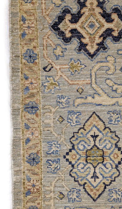 A hand-knotted wool rug with a coastal palette of beige, navy, rosy pink, blue, gold, and ivory colors, featuring intricate traditional and contemporary patterns.