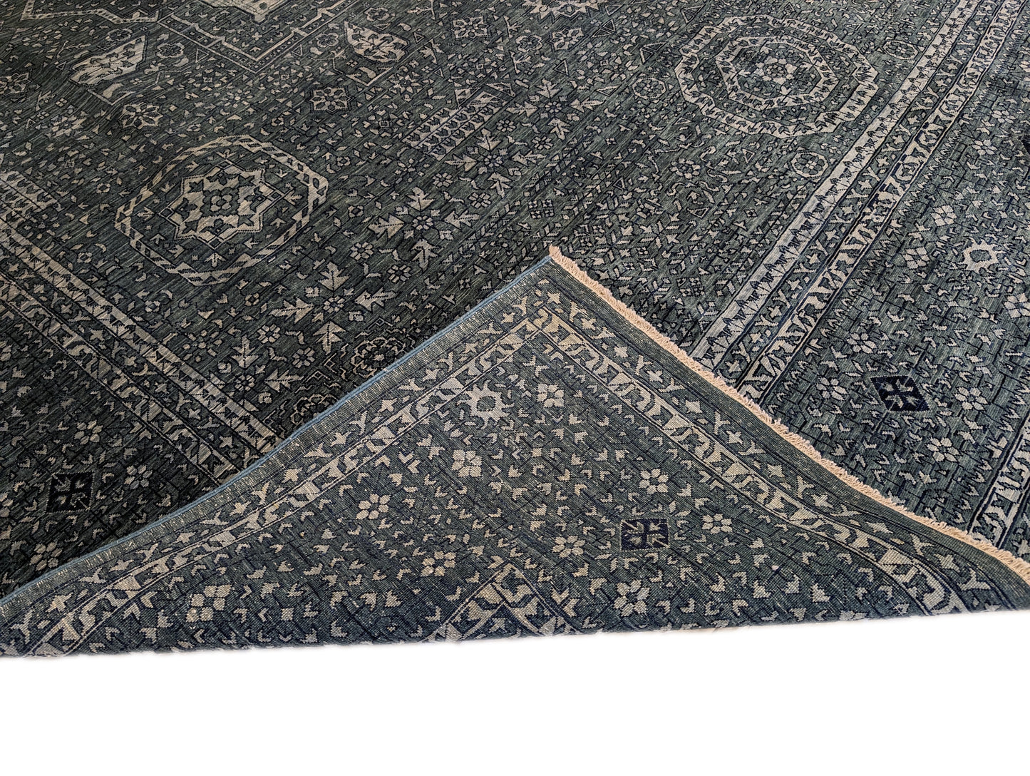 A hand-knotted wool rug with a geometric pattern in smokey green, deep navy, and crisp ivory colors.