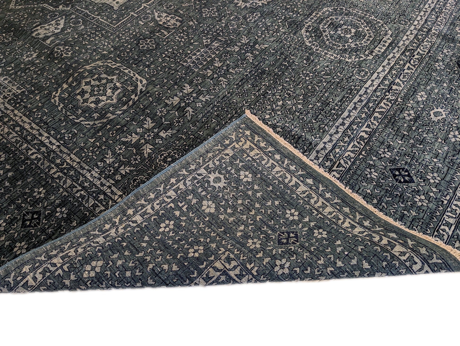 A hand-knotted wool rug with a geometric pattern in smokey green, deep navy, and crisp ivory colors.