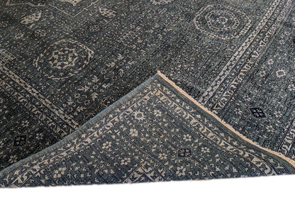A hand-knotted wool rug with a geometric pattern in smokey green, deep navy, and crisp ivory colors.