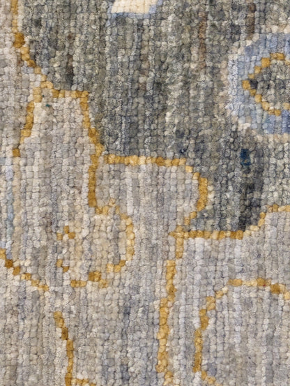 A hand-knotted wool rug with a coastal design in shades of beige, blue, brown, gold, ivory, navy, and sandy grey.