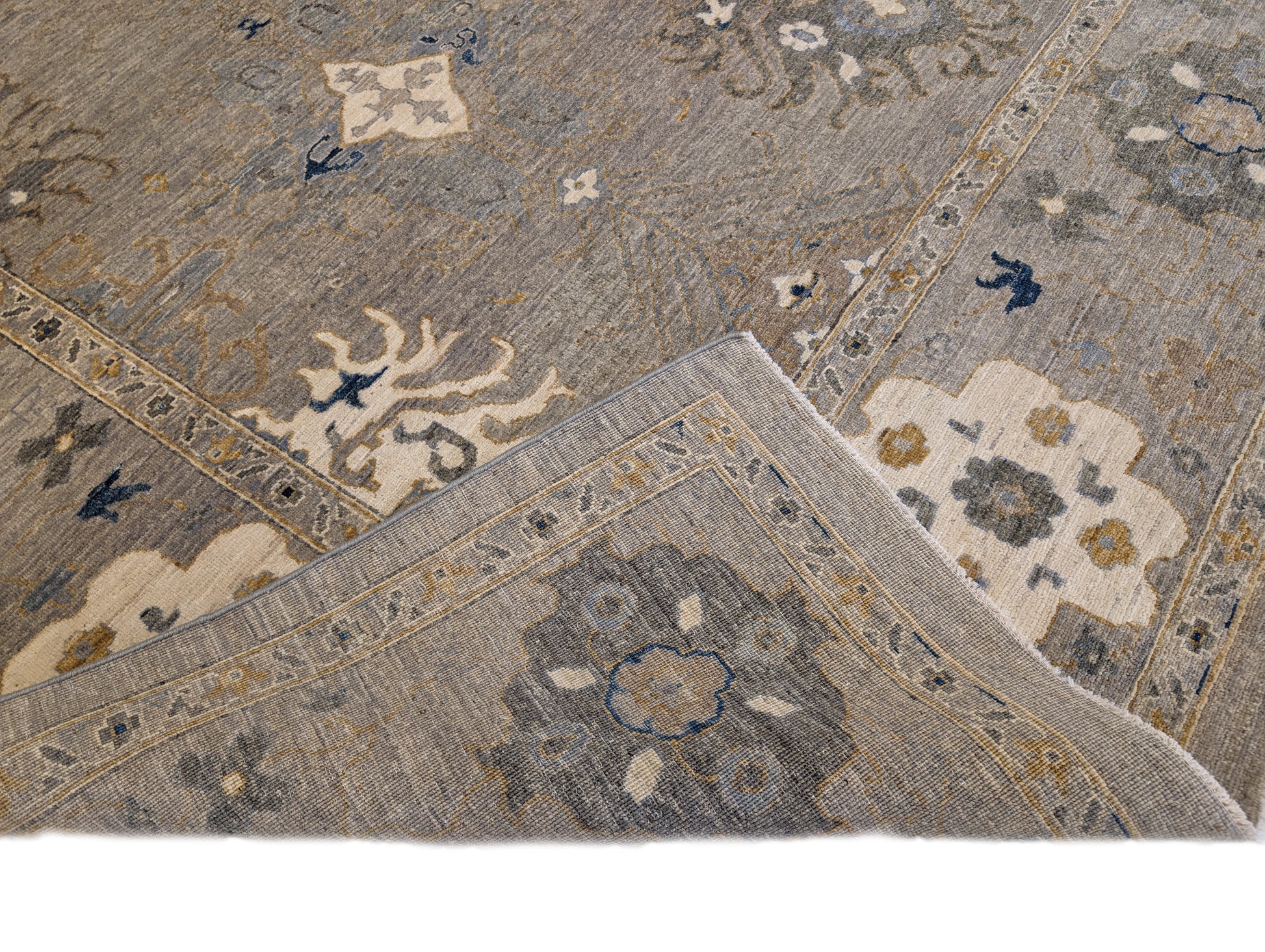 A hand-knotted wool rug with a coastal design in shades of beige, blue, brown, gold, ivory, navy, and sandy grey.