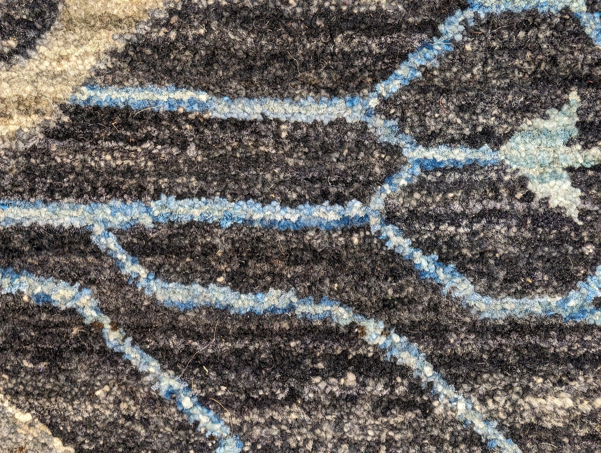 A hand-knotted wool rug with a complex pattern featuring coastal hues of navy, grey, blue, and ivory, and traditional motifs.