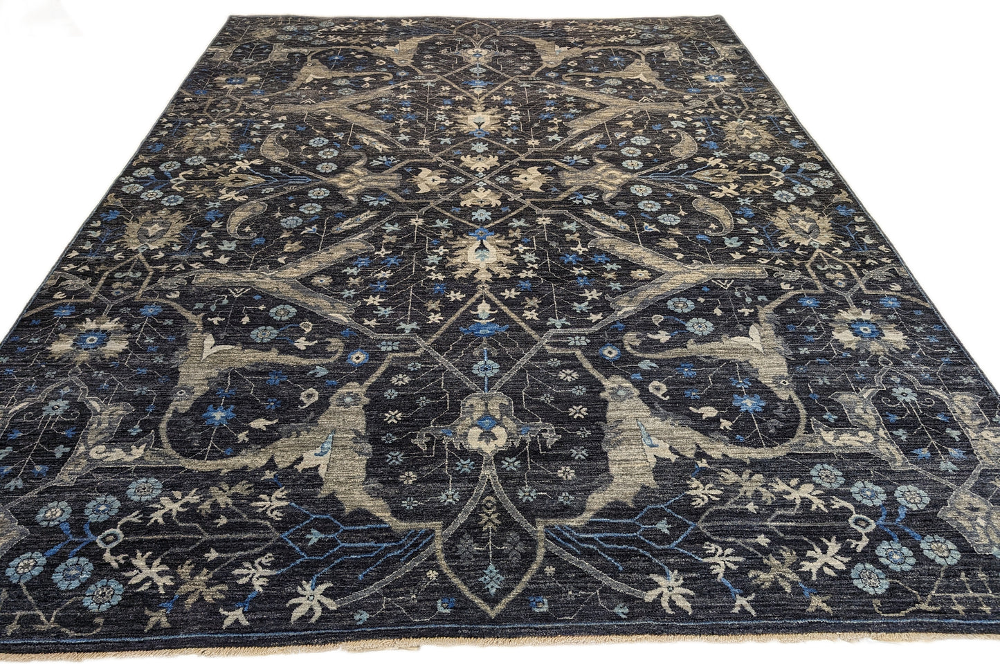 A hand-knotted wool rug with a complex pattern featuring coastal hues of navy, grey, blue, and ivory, and traditional motifs.