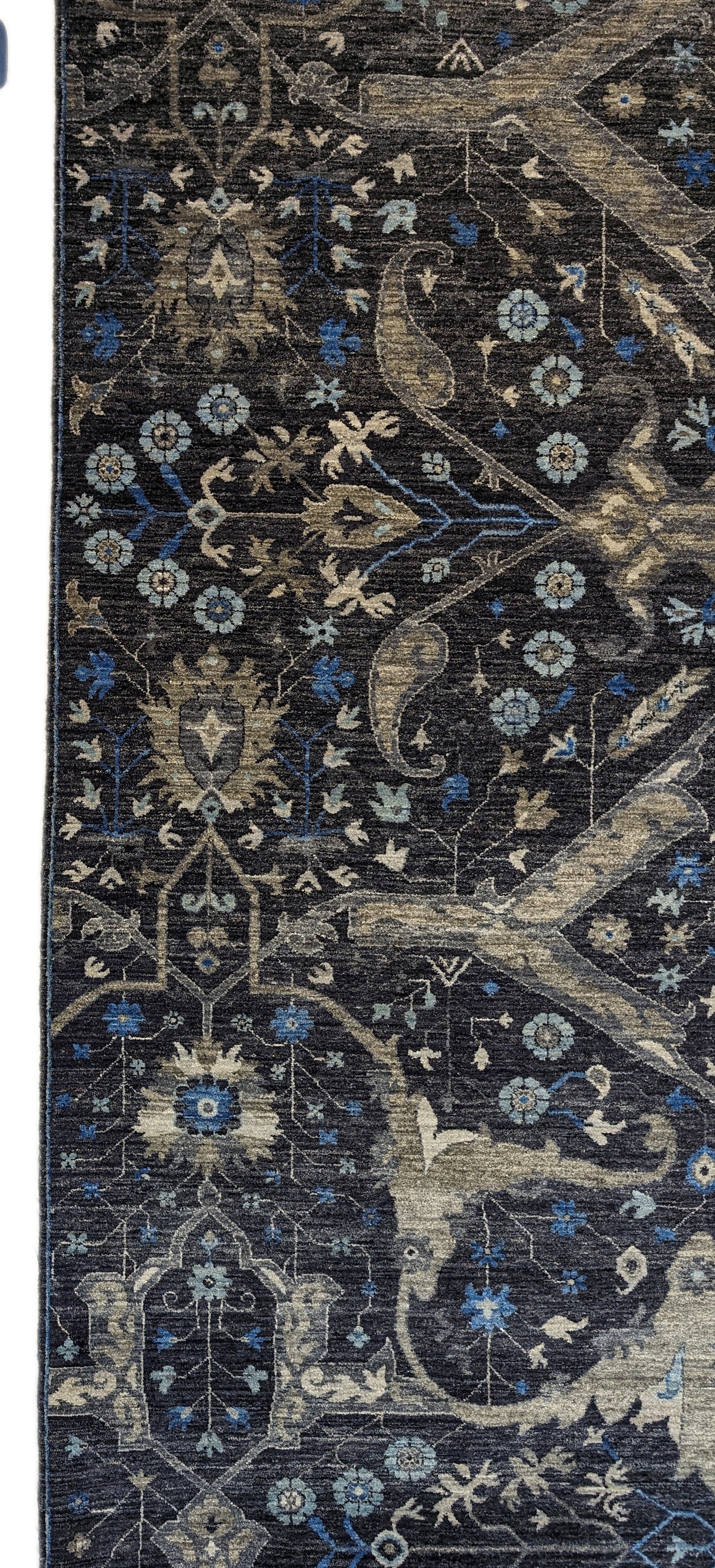 A hand-knotted wool rug with a complex pattern featuring coastal hues of navy, grey, blue, and ivory, and traditional motifs.